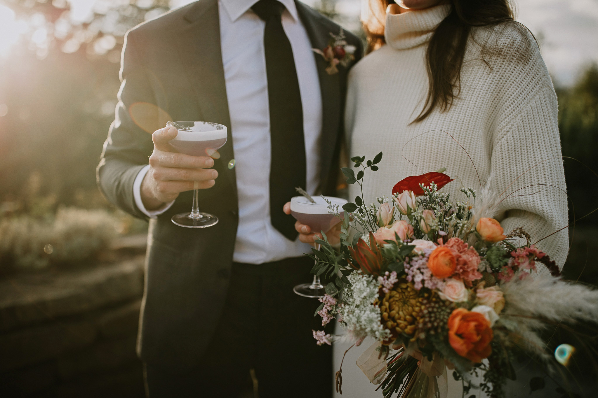 In tight shot of a fall wedding couple holding a couple of signature cocktails with a golden sunset behind