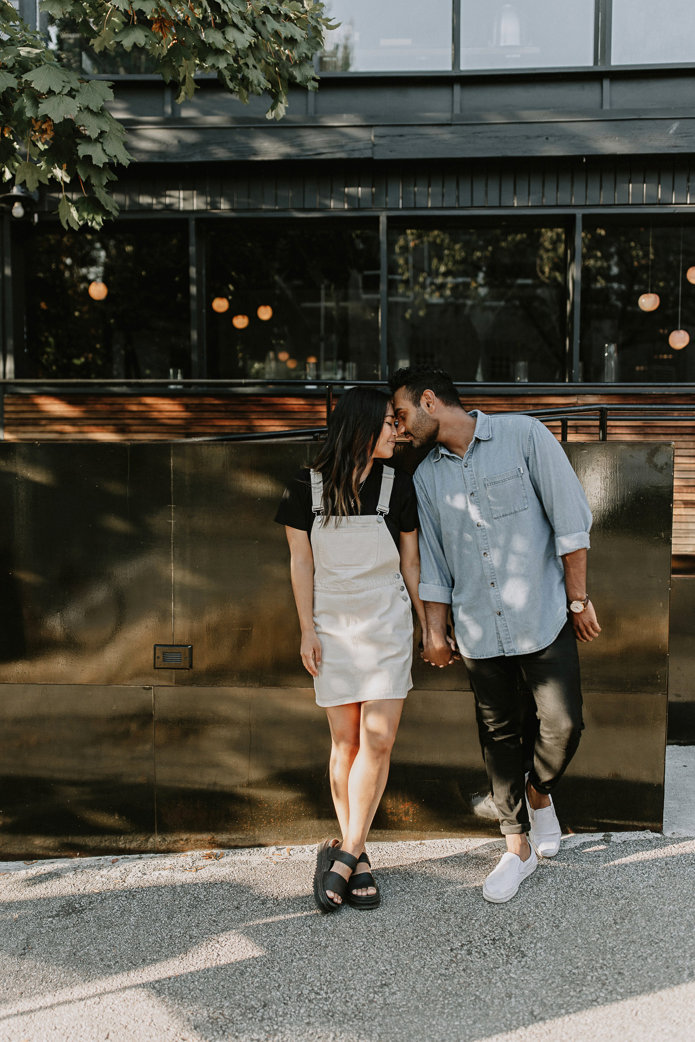 Couple standing holding hands and kissing leaning against a railing in front of a restaurant