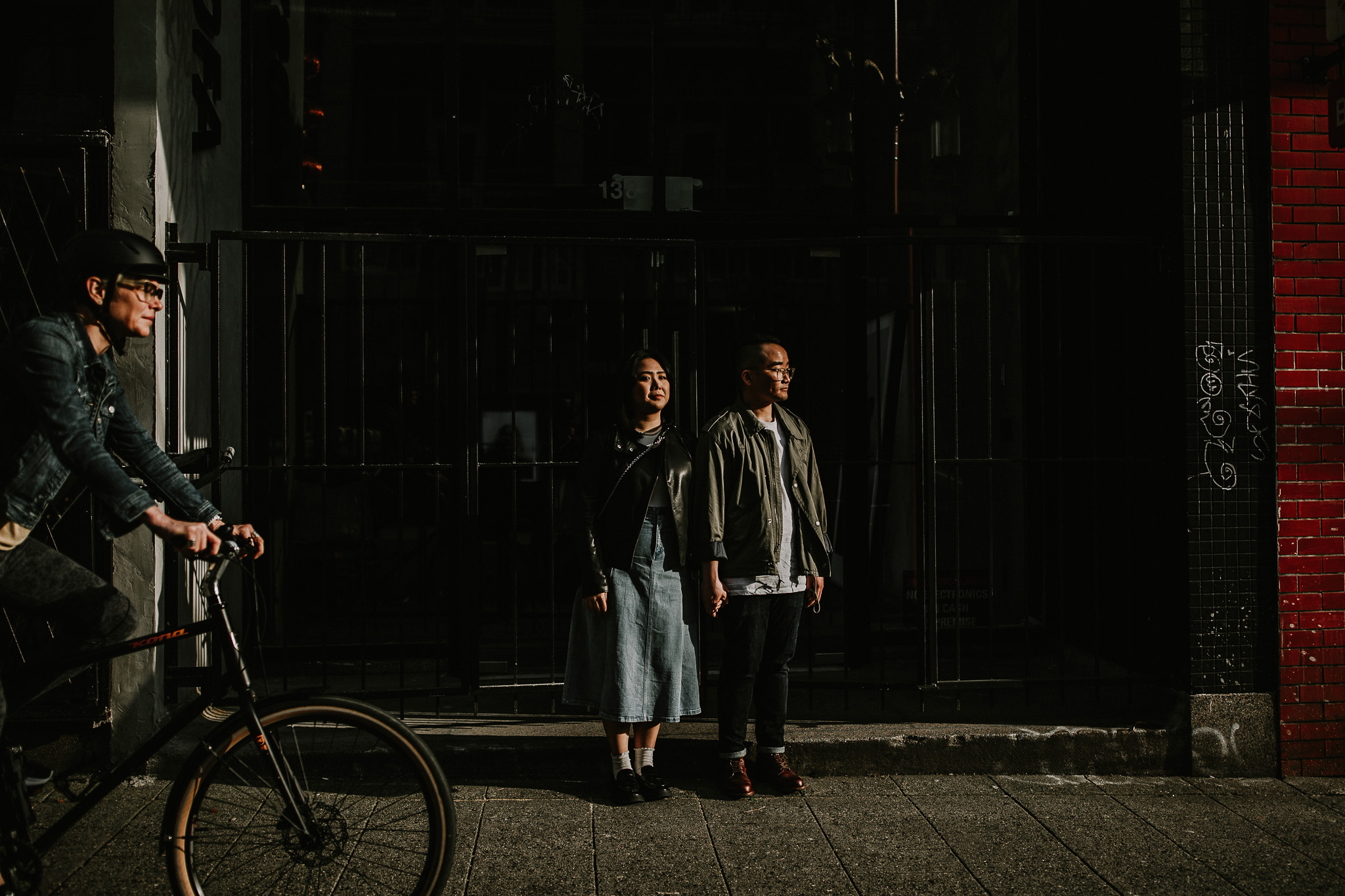 Couple standing on sidewalk at sunset in chinatown with a pedestrian biking past in the forground