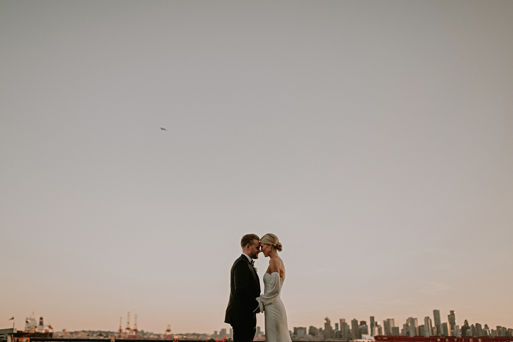 couple on their wedding day facing each other at sunset in front of the Wallace Venue in North Vancouver with downtown vancouver in the background.