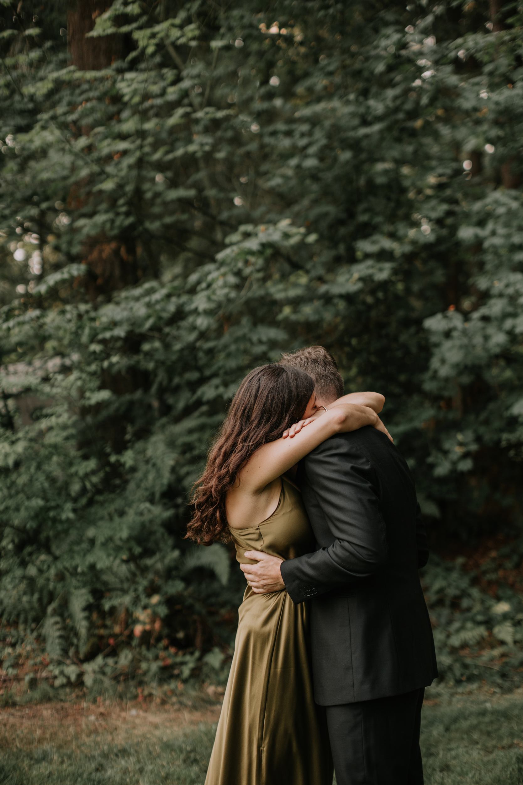 Non traditional attire wedding couple emotionally embrace during their first look in front of a lush green tree.