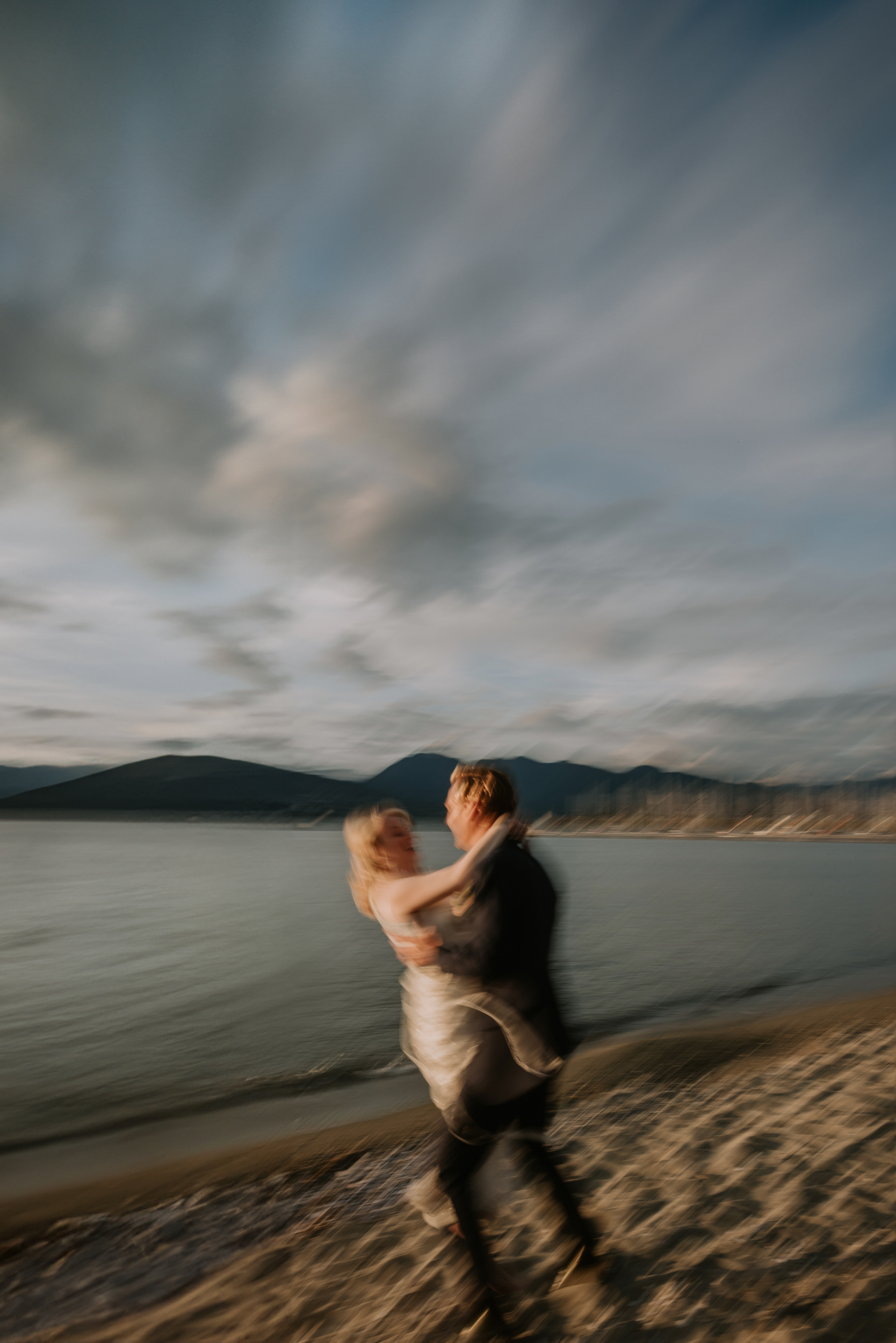 Slow shutter golden hour photo of groom spinning around and sweeping his wife off the ground.