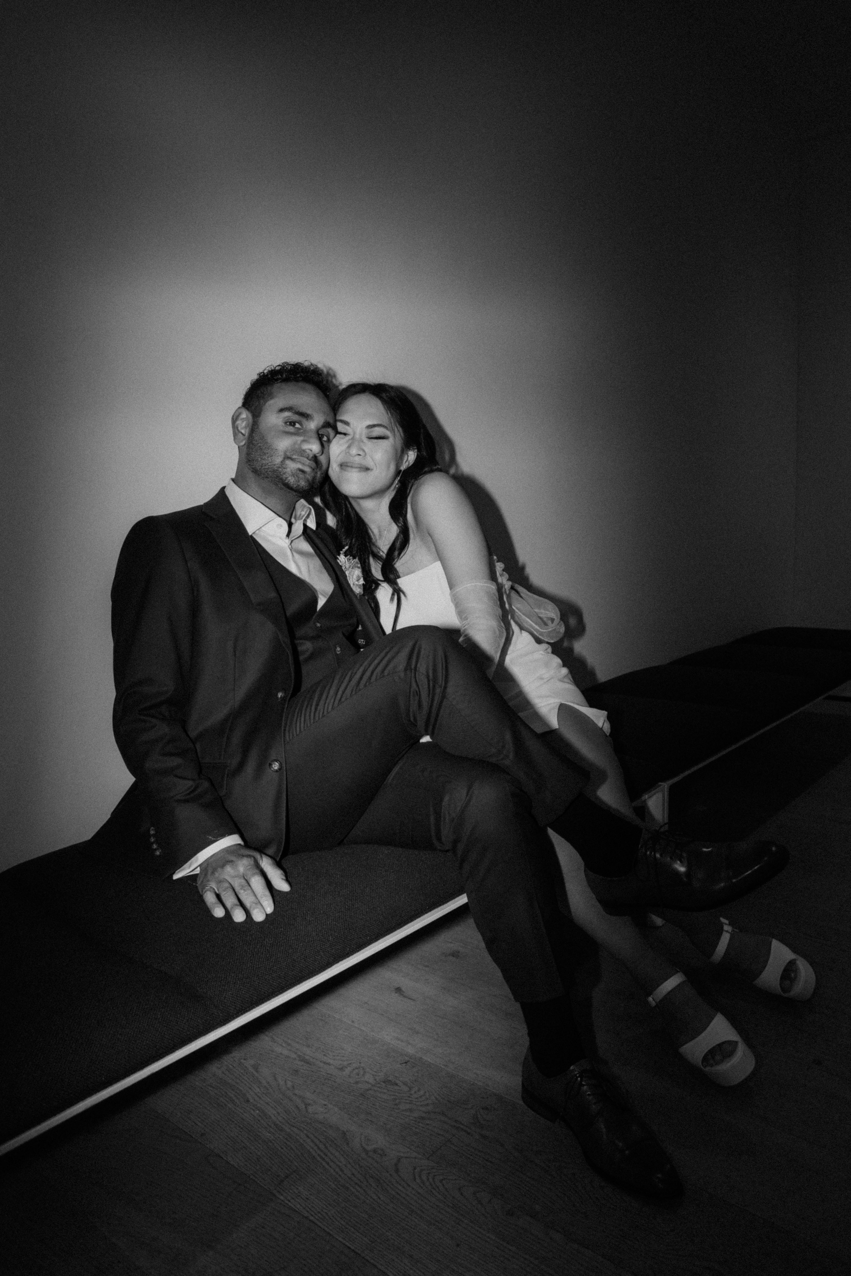 Black and white photo captured with direct flash of couple sitting down cuddling at the end of the night of their wedding